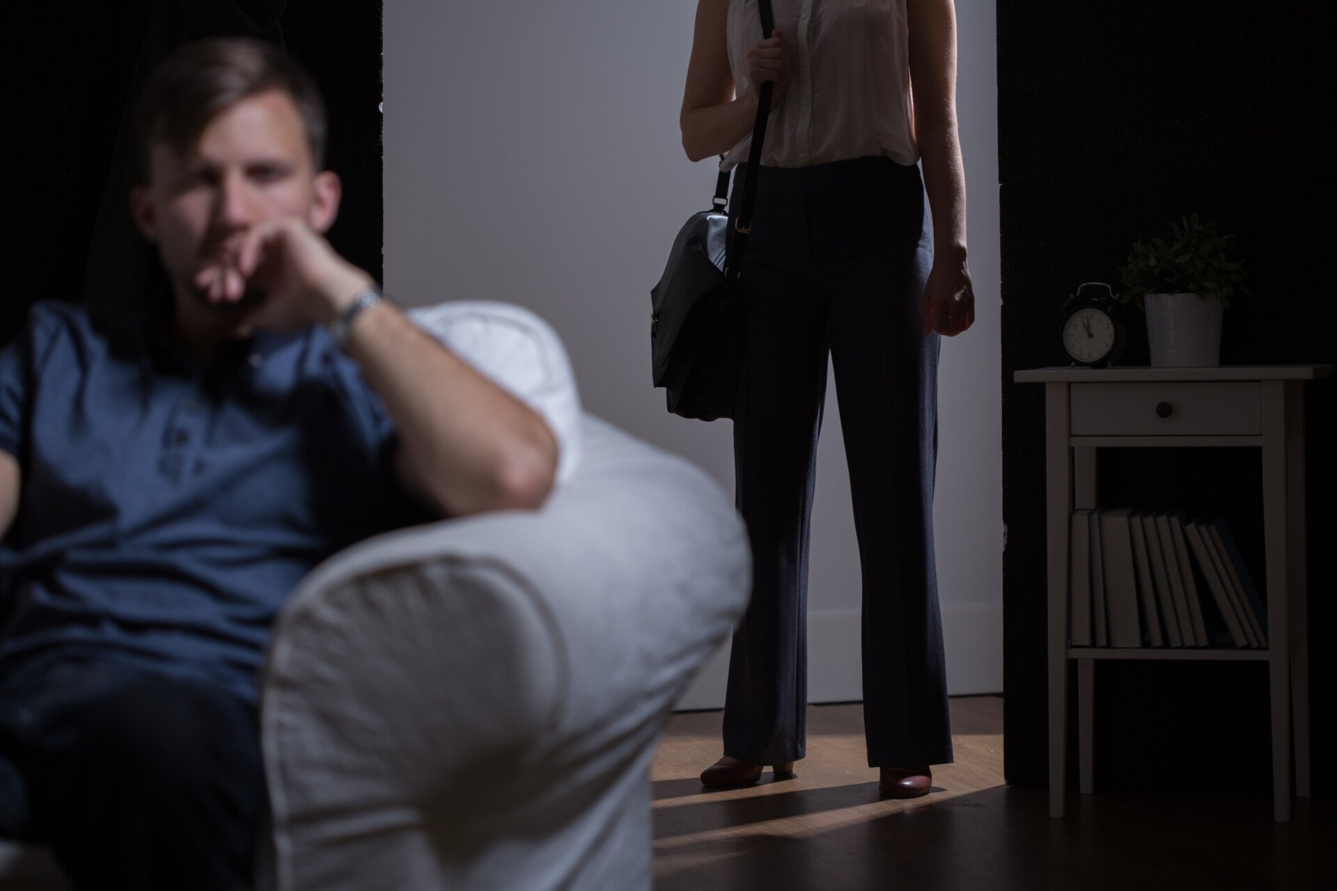 a woman stood in the doorway looking at her partner. She's holding a bag about to leave the relationship