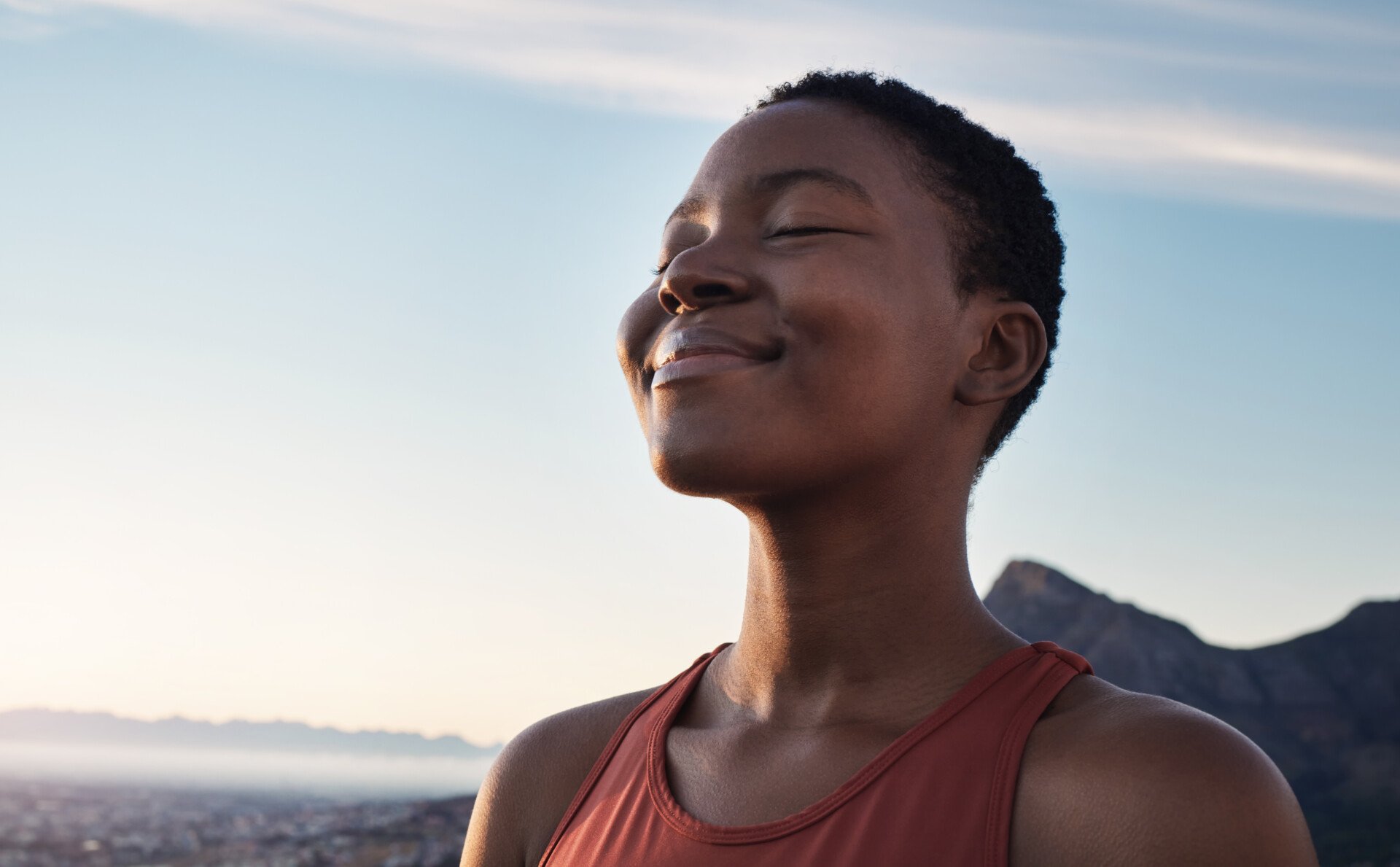 a woman outside, taking a deep breath, eyes closed and smiling