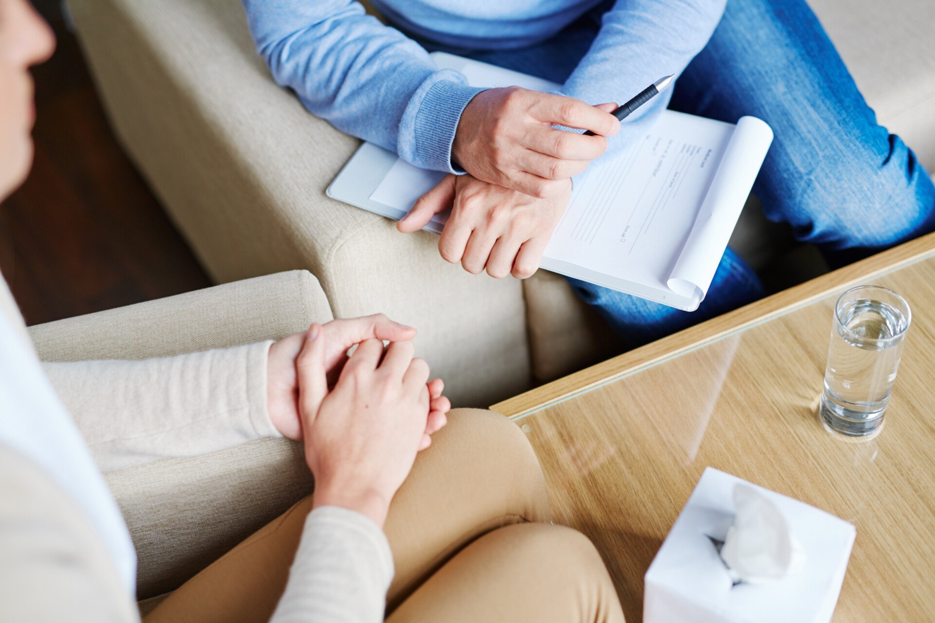 a close up of a therapist and client talking to each other. the therapist is holding a notepad and pen.