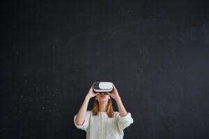 The girl in white stands on a black background in the virtual reality helmet