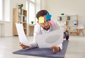a man lay on the floor reading documents with post-it notes on his head